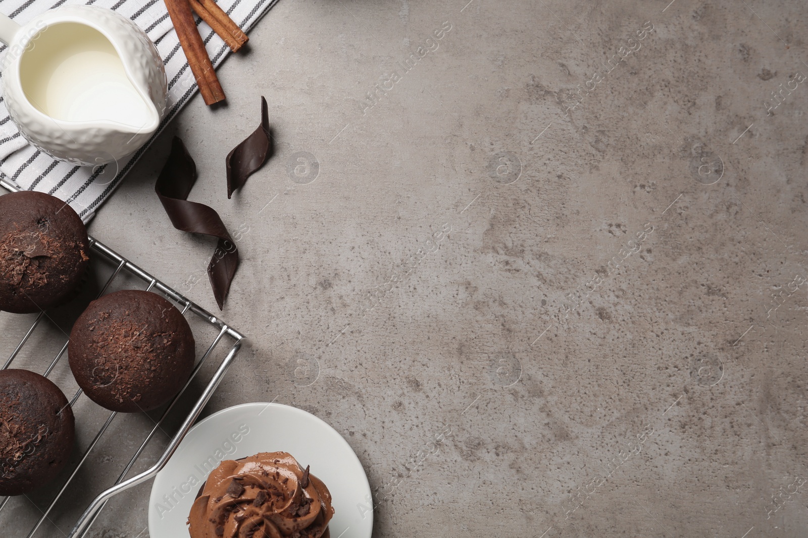 Photo of Delicious chocolate muffins and cupcake decorated with cream on grey table, flat lay. Space for text