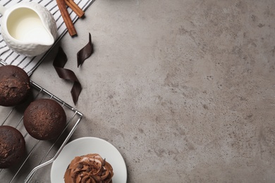 Photo of Delicious chocolate muffins and cupcake decorated with cream on grey table, flat lay. Space for text