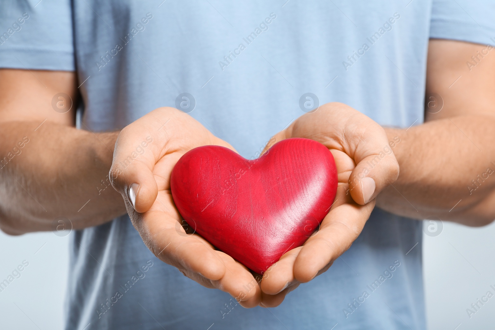 Photo of Young man holding red heart on color background, closeup. Donation concept