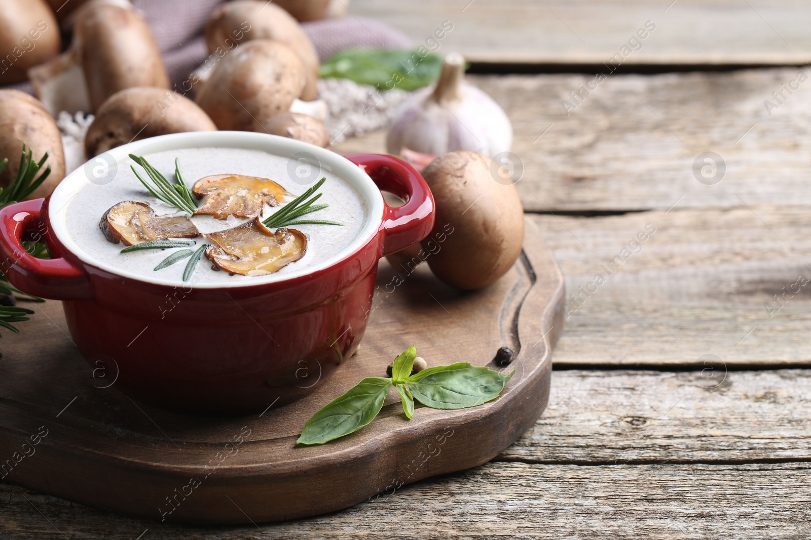 Photo of Delicious homemade mushroom soup in ceramic pot and fresh ingredients on wooden table. Space for text