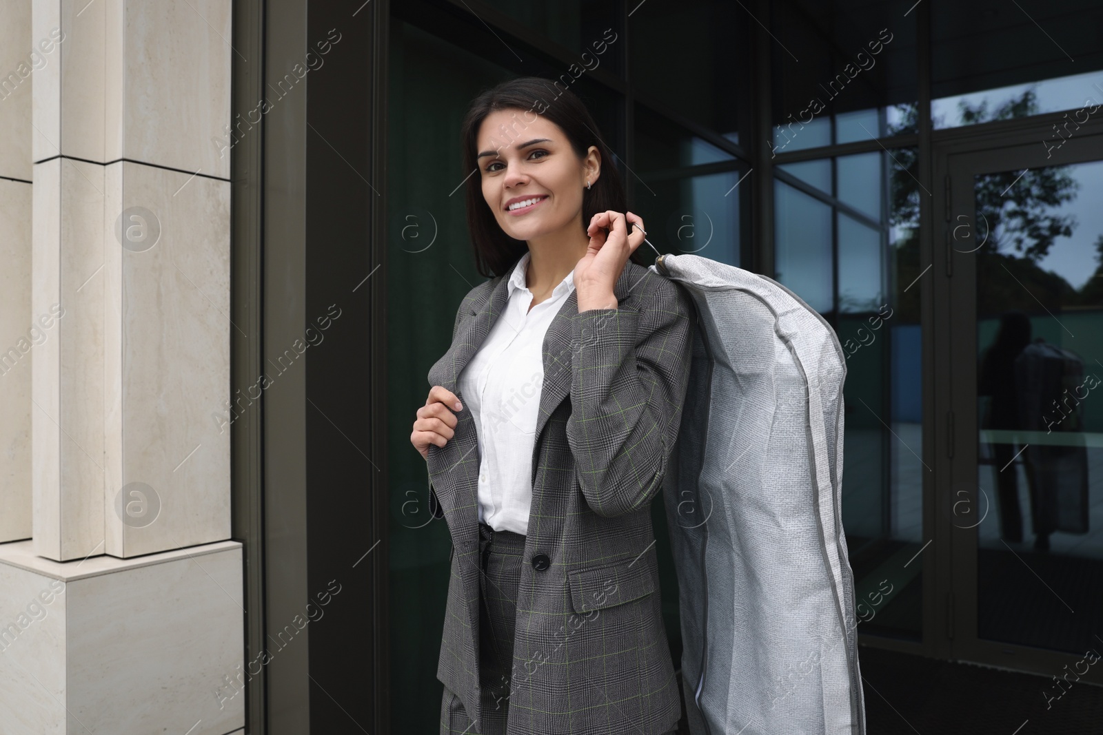 Photo of Attractive happy businesswoman holding garment cover with clothes outdoors. Dry cleaning service