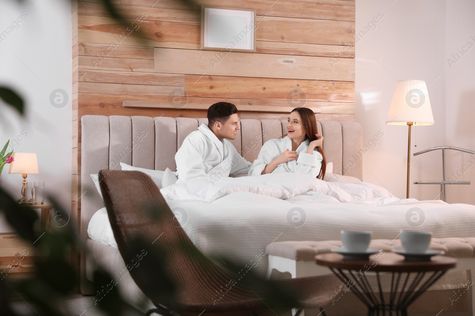 Photo of Happy couple in bathrobes resting on bed at home