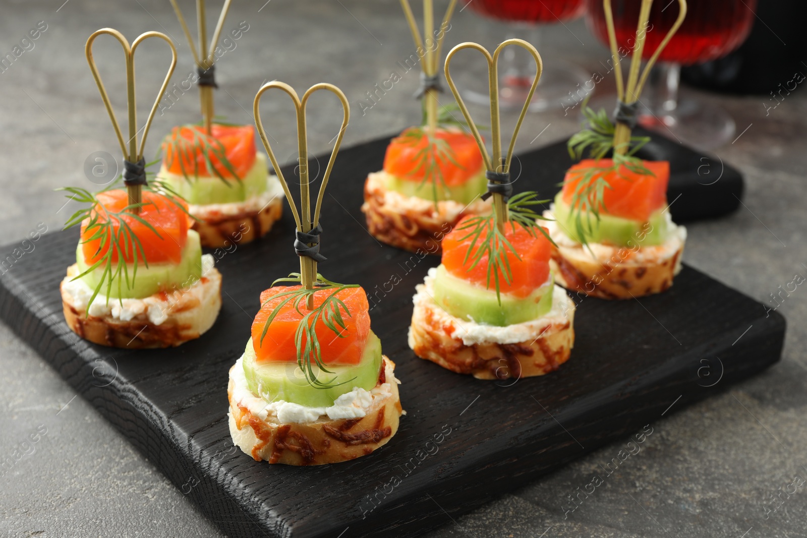 Photo of Tasty canapes with salmon, cucumber, bread and cream cheese on grey table, closeup