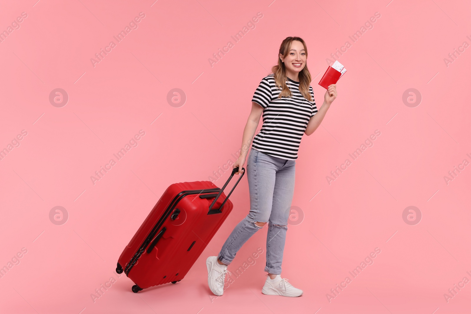 Photo of Happy young woman with passport, ticket and suitcase on pink background