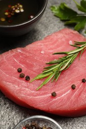 Photo of Raw tuna fillet with herbs and spices on gray table, closeup