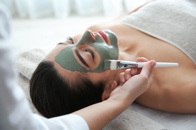 Photo of Cosmetologist applying mask on client's face in spa salon