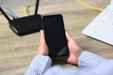 Photo of Woman with smartphone connecting to internet via Wi-Fi router at wooden table indoors, closeup