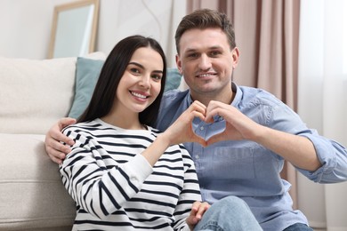 Happy couple making heart with hands at home