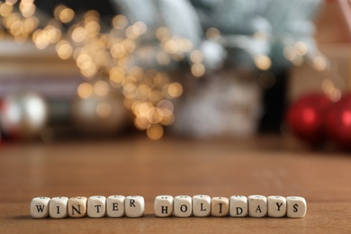 Photo of Cubes with phrase Winter Holidays and blurred Christmas decor on background. Space for text