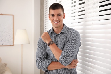 Photo of Portrait of handsome young man near window blinds indoors