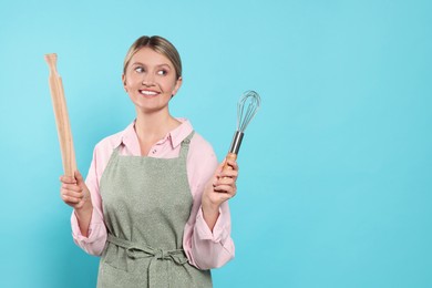 Photo of Beautiful young woman in clean apron with kitchen tools on light blue background. Space for text