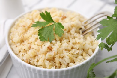 Photo of Cooked bulgur with parsley in bowl on white table, closeup