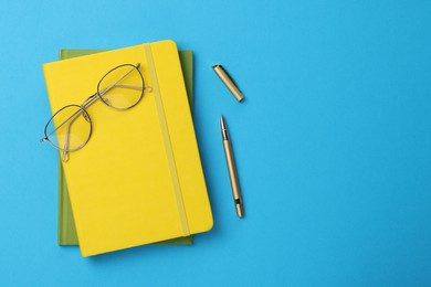 Photo of Ballpoint pen, notebooks and glasses on light blue background, flat lay. Space for text