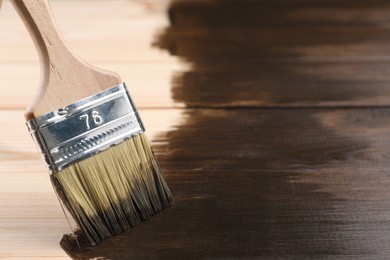 Photo of Applying wood stain with brush onto wooden surface, closeup. Space for text