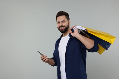 Happy man with many paper shopping bags and smartphone on grey background. Space for text