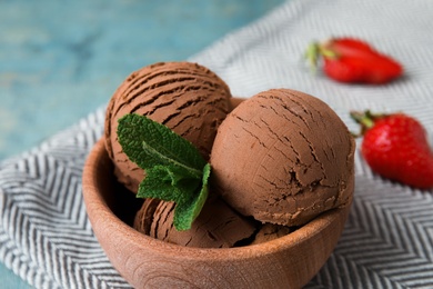 Photo of Wooden bowl of chocolate ice cream, mint and strawberry on table, closeup