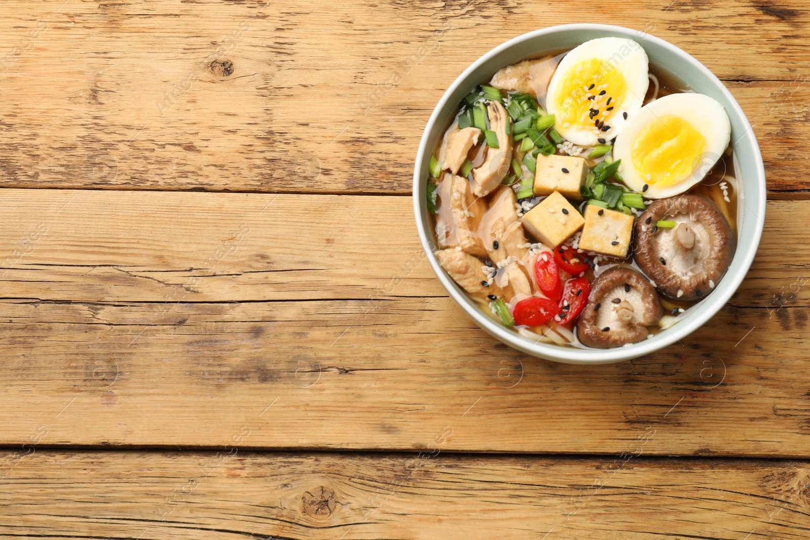 Photo of Bowl of delicious ramen on wooden table, top view with space for text. Noodle soup