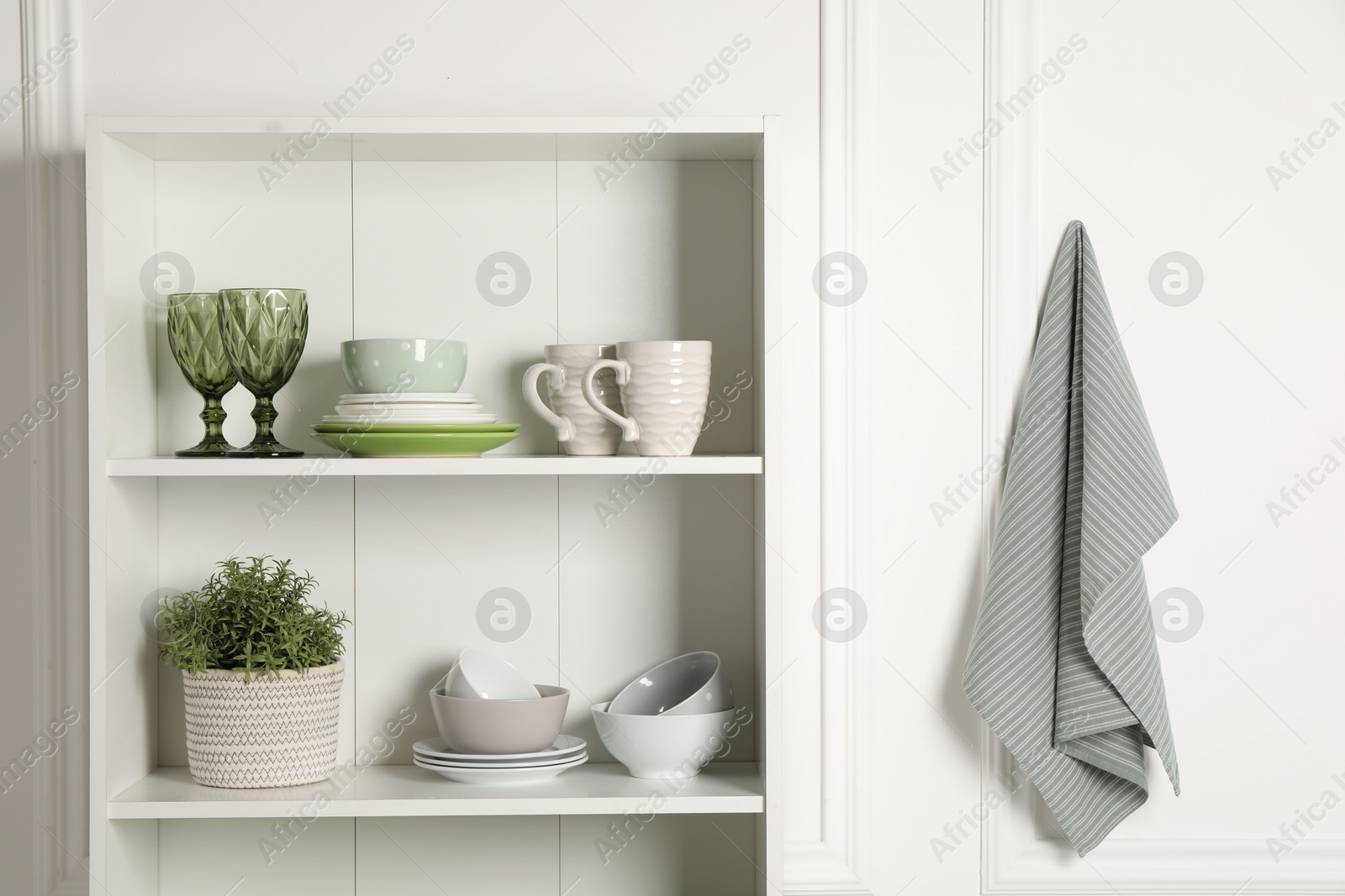 Photo of Different clean dishware and houseplant on shelves in cabinet indoors