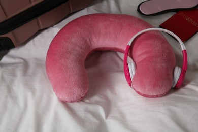 Photo of Pink travel pillow with headphones, suitcase, passport and sleep mask on bed