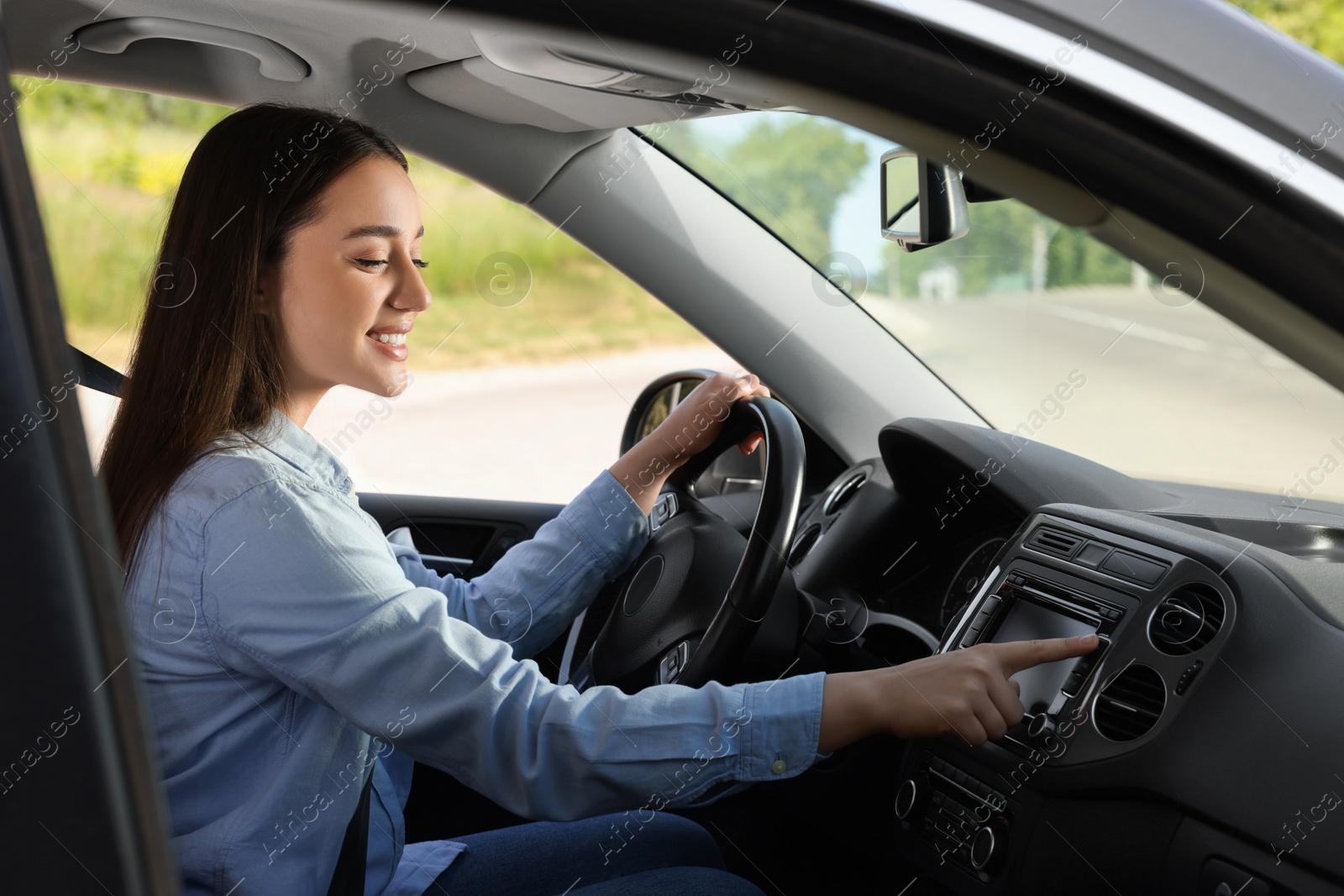 Photo of Choosing favorite radio. Beautiful young woman pressing button on vehicle audio in car