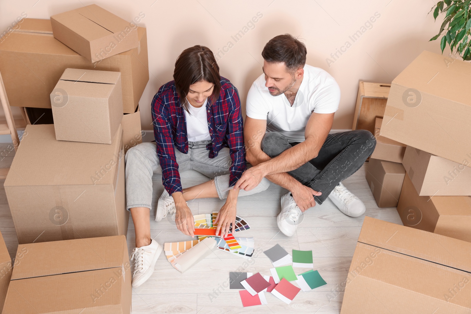 Photo of Happy couple surrounded by moving boxes choosing colors in new apartment, above view