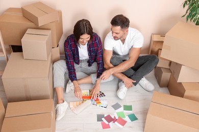 Happy couple surrounded by moving boxes choosing colors in new apartment, above view