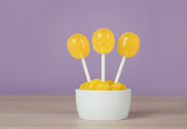 Photo of Delicious lemon drops and lollipops on wooden table against lilac background