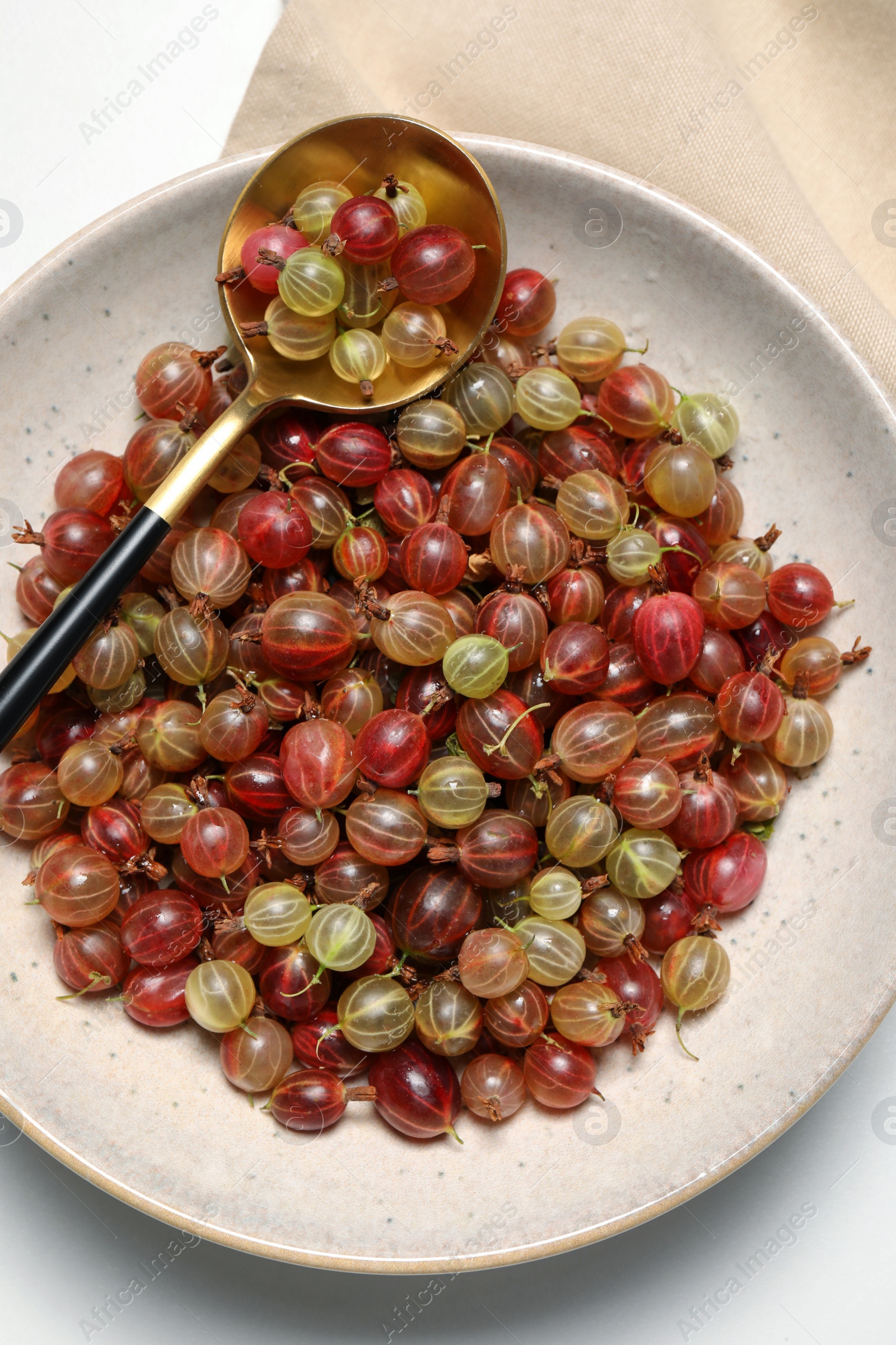 Photo of Plate of fresh ripe gooseberries and spoon on white table, top view