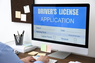Photo of Man using computer to fill driver's license application form at table in office, closeup