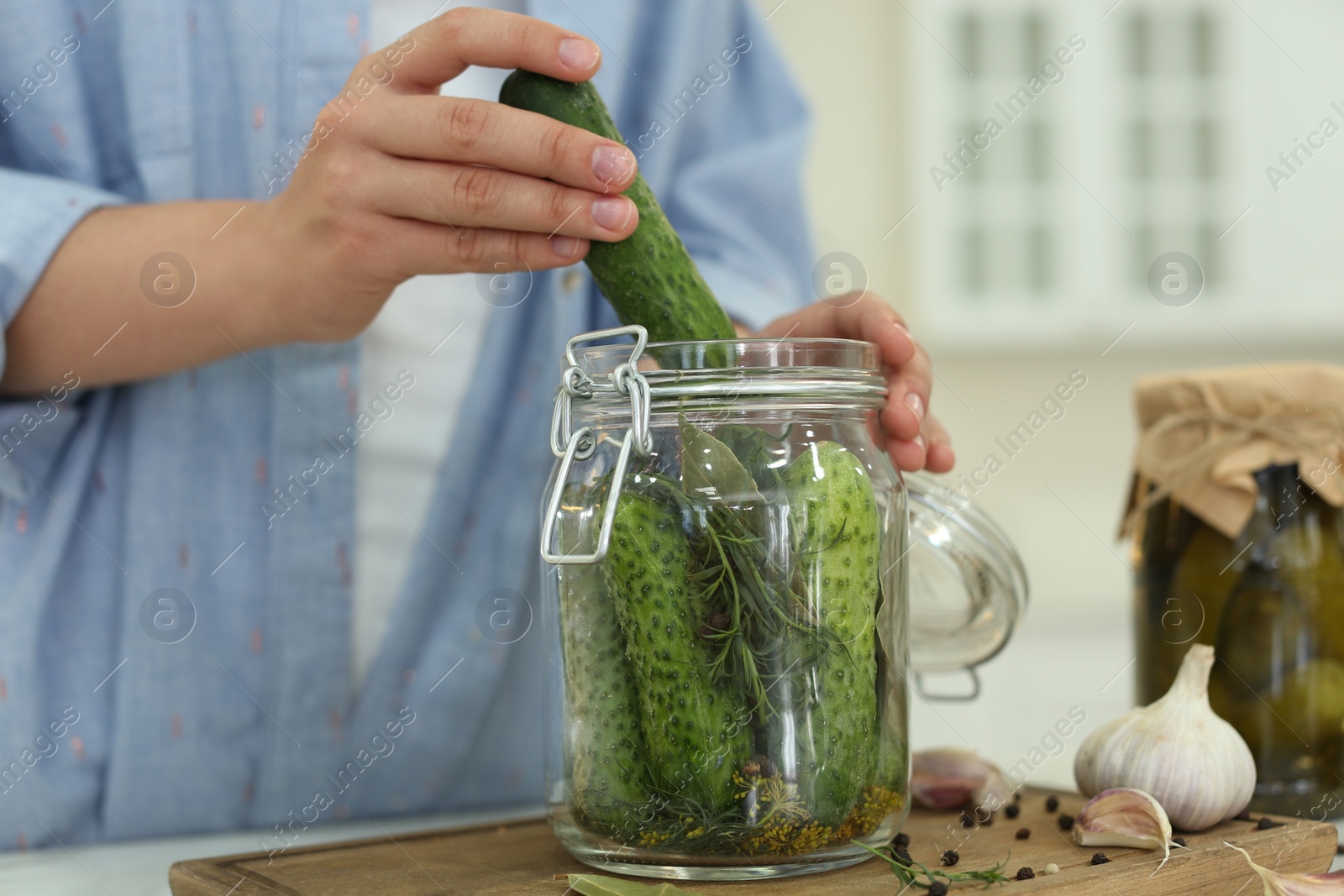 Photo of Woman putting cucumber into pickling jar at table in kitchen, closeup