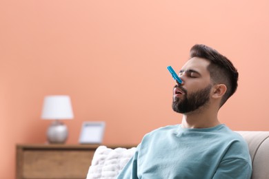 Photo of Man with clothespin suffering from runny nose at home. Space for text