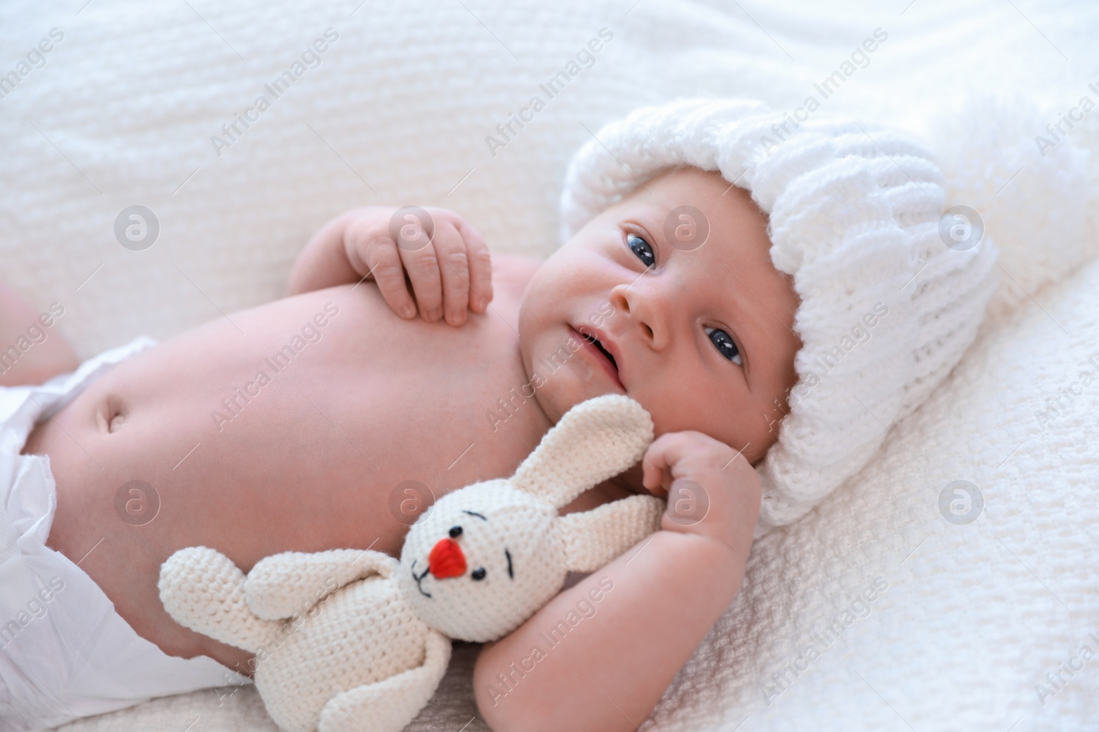 Photo of Cute newborn baby with toy in white knitted hat on plaid