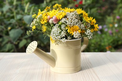 Photo of Beautiful bouquet of bright wildflowers in watering can on white wooden table outdoors