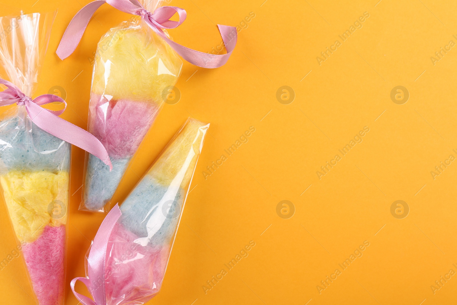 Photo of Packaged sweet cotton candies on orange background, flat lay. Space for text