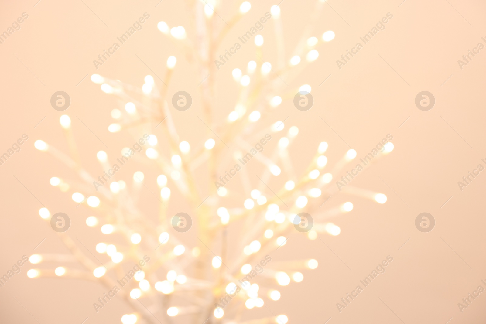 Photo of Decorative tree with lights on beige background, blurred view