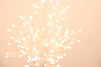 Photo of Decorative tree with lights on beige background, blurred view