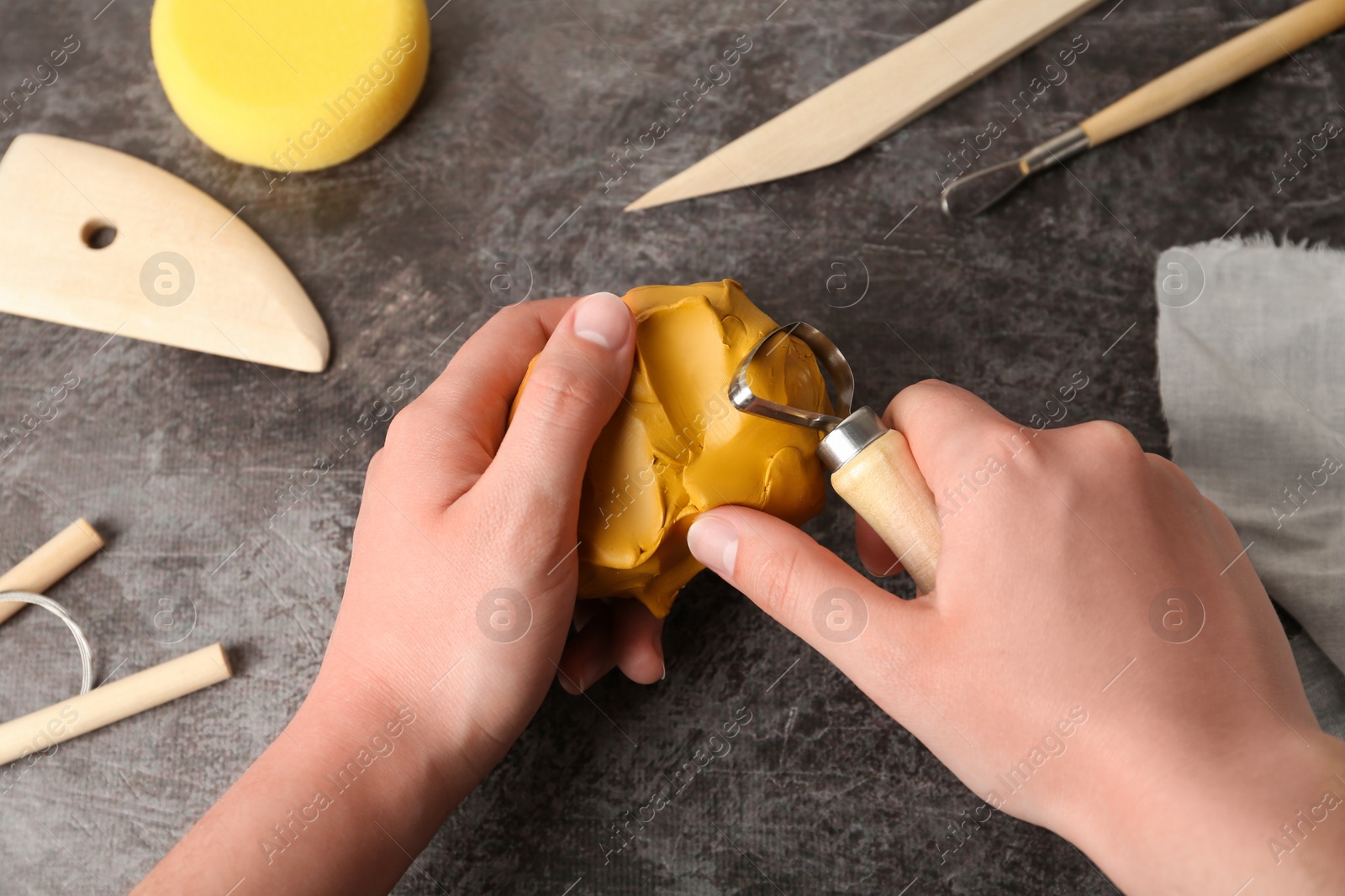 Photo of Woman working with loop tool and clay at grey stone table, closeup