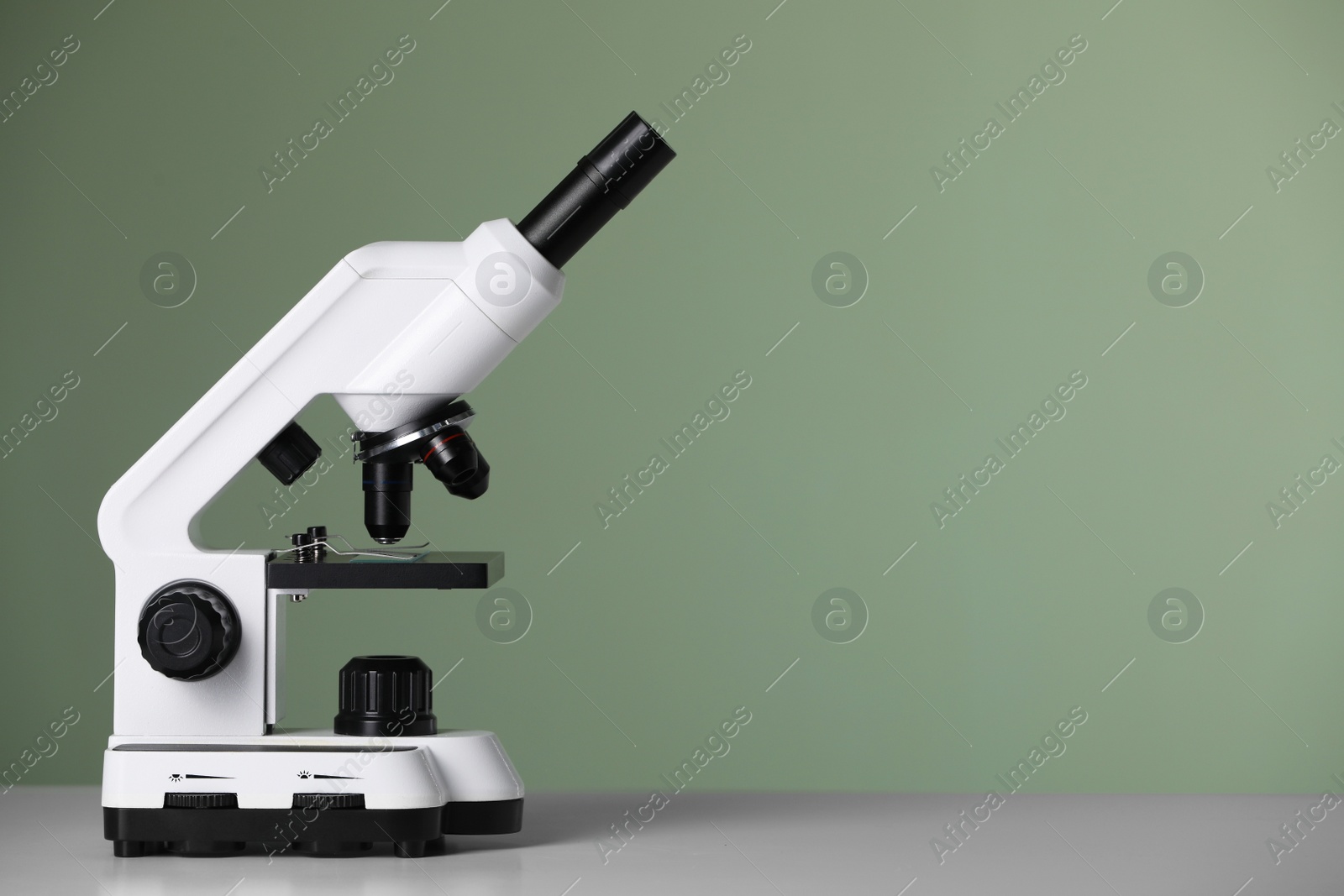 Photo of Modern microscope on table against green background. Space for text