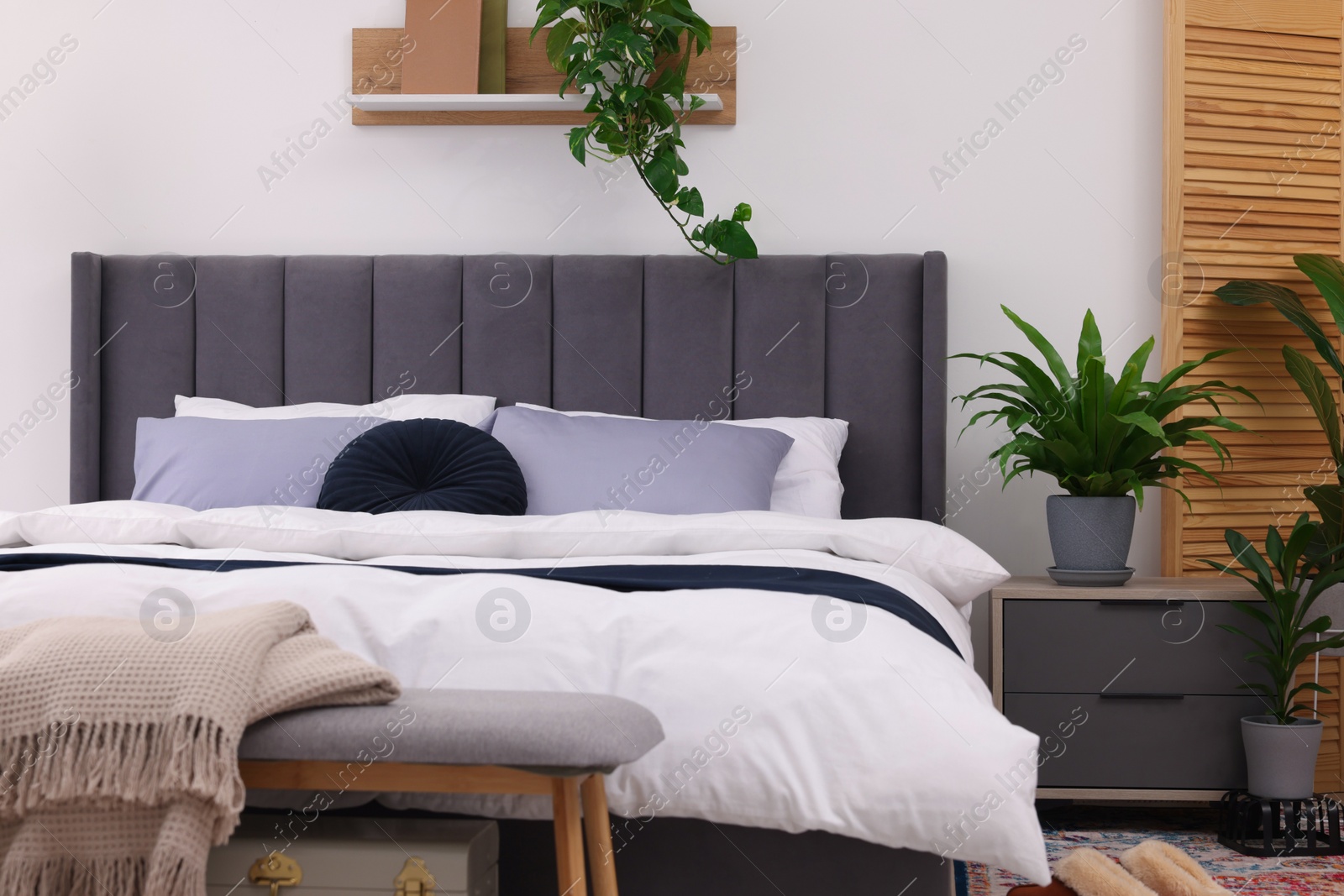 Photo of Beautiful green houseplants and bed in room. Bedroom interior