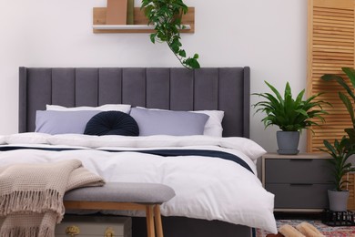 Photo of Beautiful green houseplants and bed in room. Bedroom interior