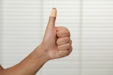 Man with sticking plaster showing thumb up indoors, closeup