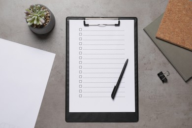 Clipboard with checkboxes, plant and office stationery on grey table, flat lay. Checklist