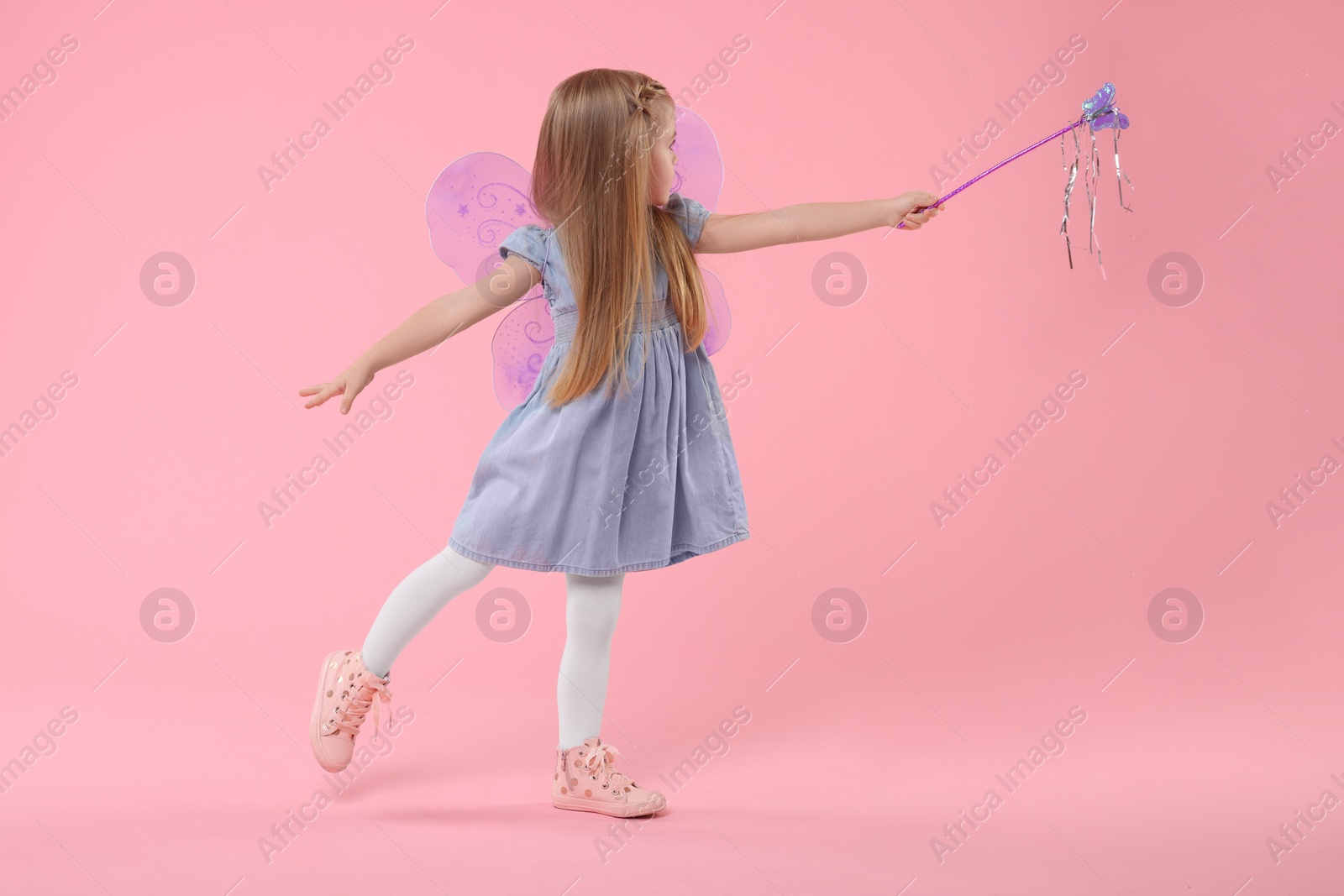 Photo of Cute little girl in fairy costume with violet wings and magic wand on pink background