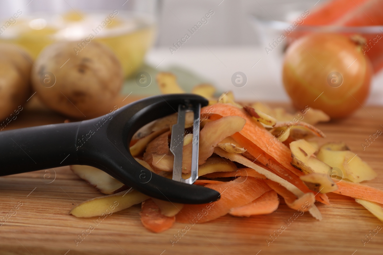 Photo of Peels of fresh vegetables and peeler on wooden table, closeup