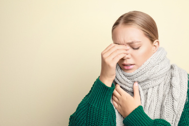 Young woman wearing scarf suffering from headache on light background, space for text. Cold symptoms