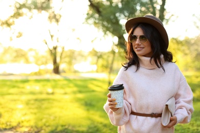 Beautiful young woman with coffee cup wearing stylish sweater in autumn park