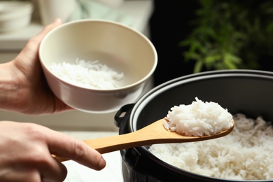 Photo of Woman putting tasty rice into bowl from cooker in kitchen, closeup