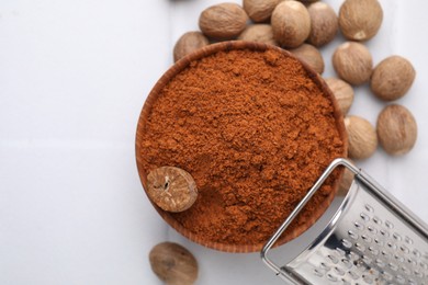 Photo of Nutmeg powder in bowl, seeds and grater on white table, flat lay. Space for text