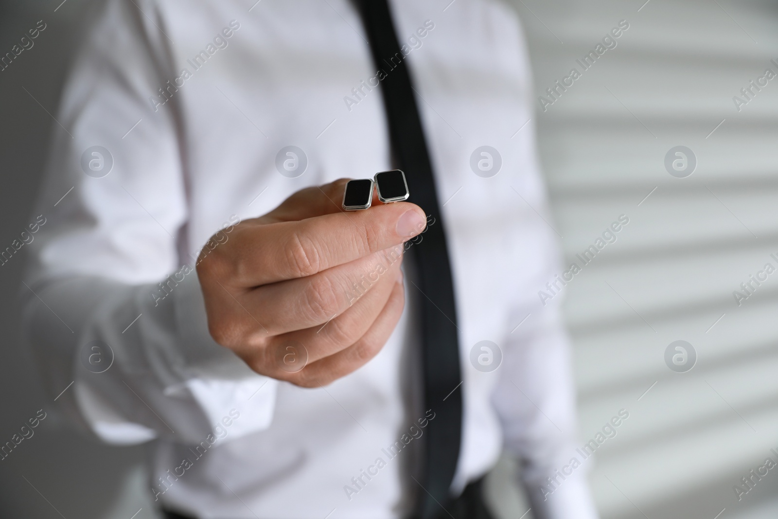 Photo of Man holding stylish cufflinks on blurred background, closeup