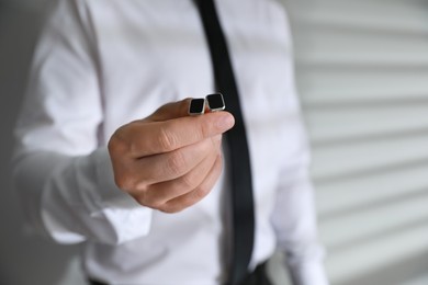 Man holding stylish cufflinks on blurred background, closeup